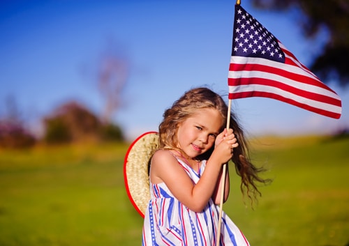 little girl in a field holding an american flag
