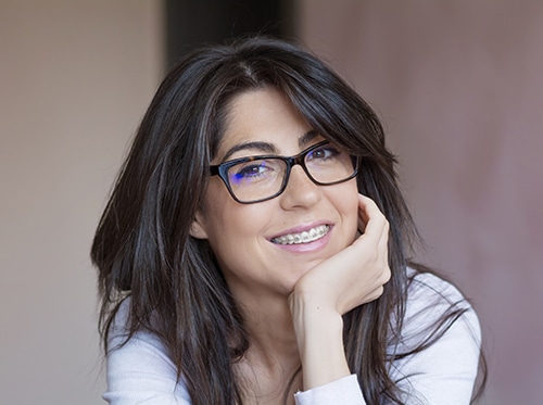 portrait of woman with dark hair, glasses, and braces smiling