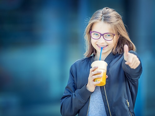 a young child smiling with a drink in her hand while giving a thumbs up