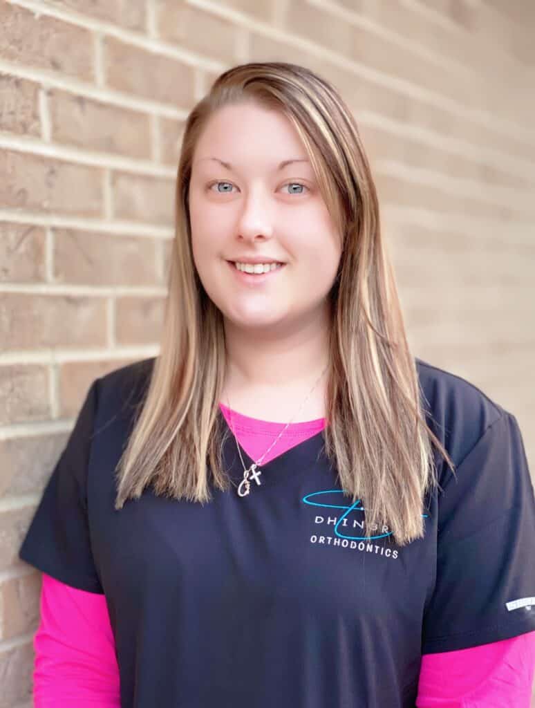 Courtney, Dhingras orthodontic assistant smiling while wearing pink and black scrubs