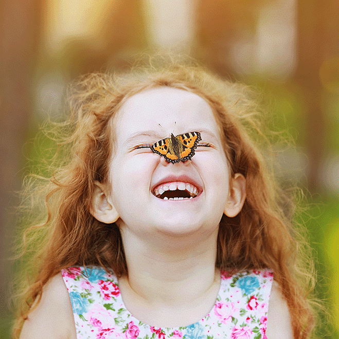 a little girl smiling with a monarch butterfly on her nose