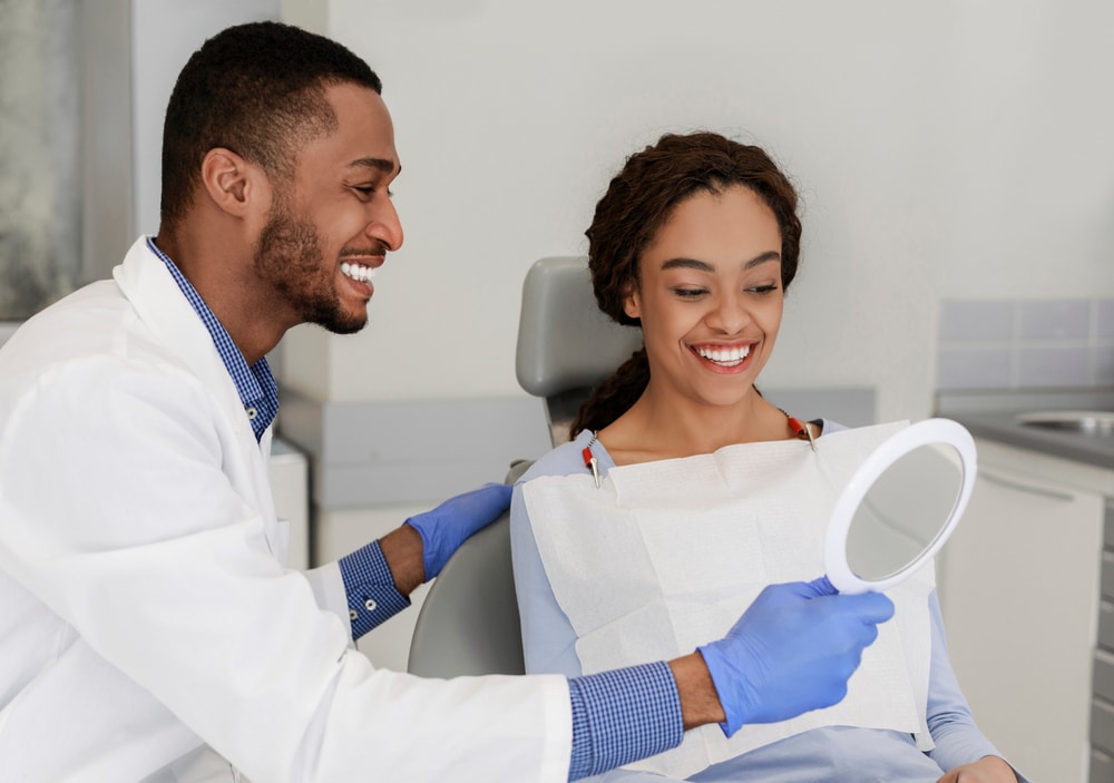 a dental assistant holding a mirror for an orthodontic patient to inspect their straight teeth