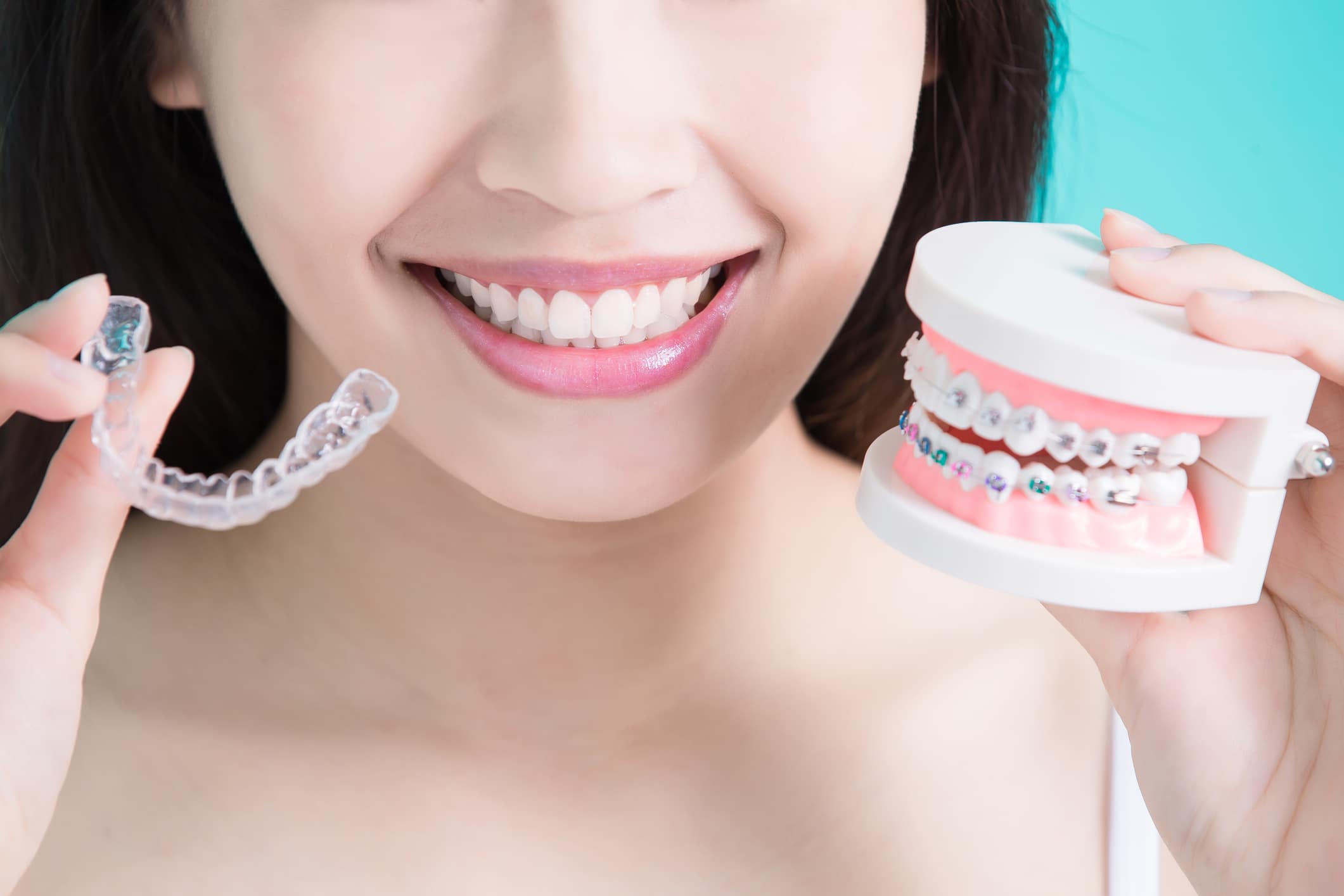 a woman holding invisalign aligners and a typodont model with braces