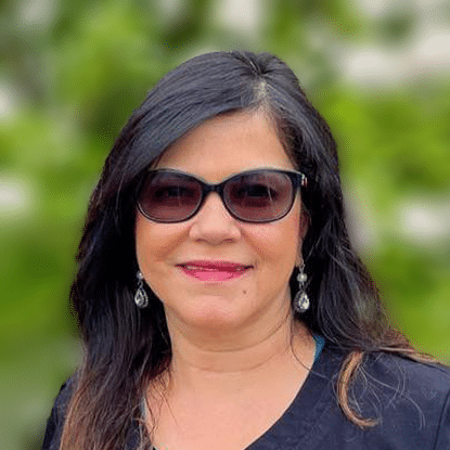 Orthodontist Dr. Seema Dhingra smiling outside in stylish red tinted sunglasses