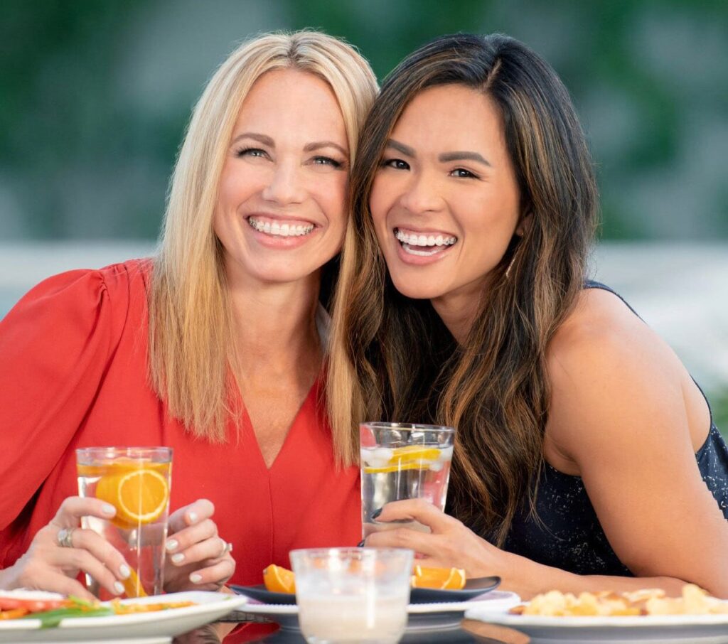 Two women with braces for adults posing for a picture as they have lunch together.