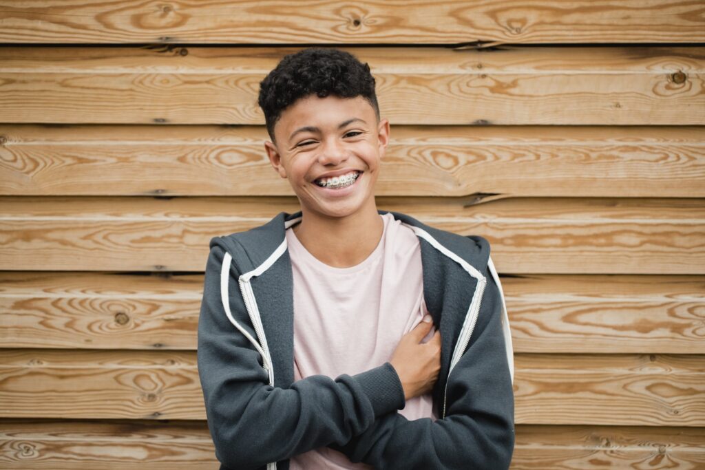 Teenager with braces teens and a beaming smile posing against an outdoor wall.