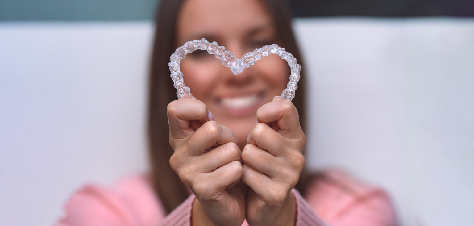 Woman with Invisalign® in Bellefontaine, Ohio holding her aligners in the shape of a heart