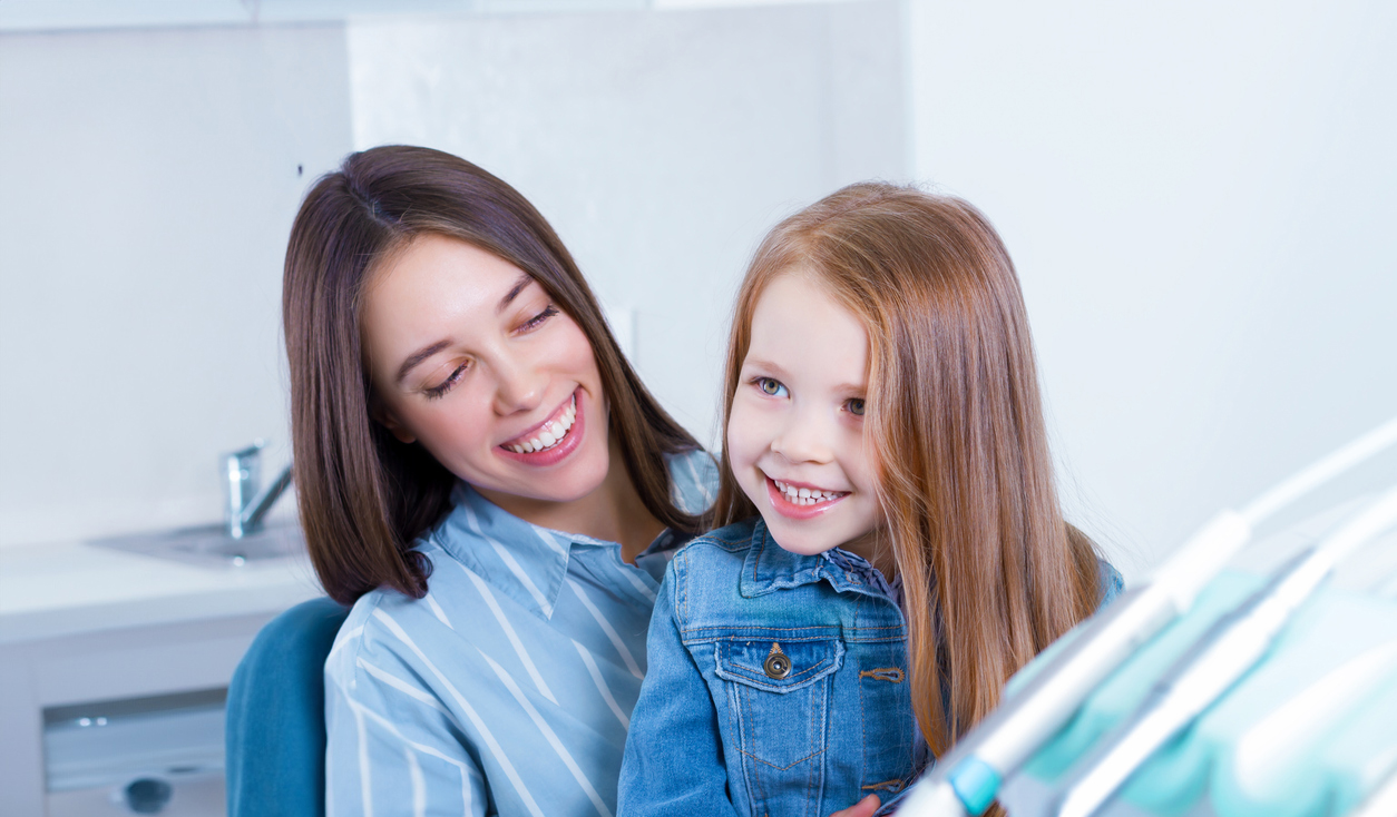 Smiling girl in her mother’s lap before receiving early orthodontic treatment in Springfield
